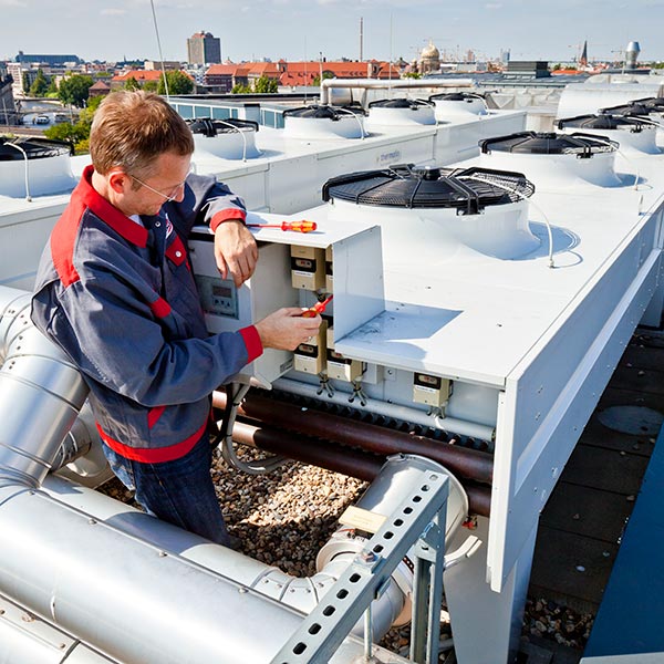 Wartung und Instandhaltung: Ein ELMATIC-Mitarbeiter kontrolliert eine Klimaanlage auf einem Dach